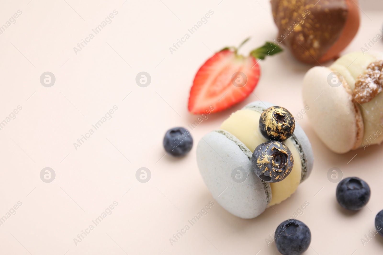 Photo of Delicious macarons and berries on beige table, closeup. Space for text