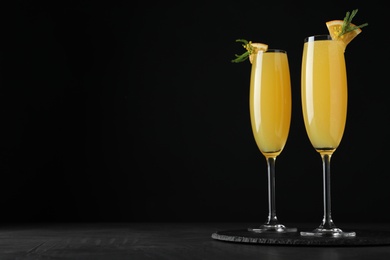 Photo of Glasses of Mimosa cocktail with garnish on black table. Space for text