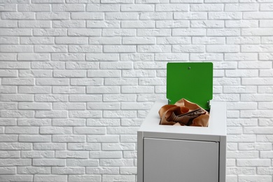 Photo of Trash bin with paper and cardboard near brick wall, space for text. Recycling concept