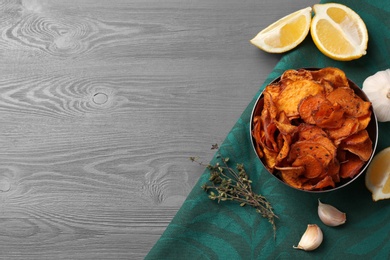 Flat lay composition with bowl of sweet potato chips and space for text on wooden table