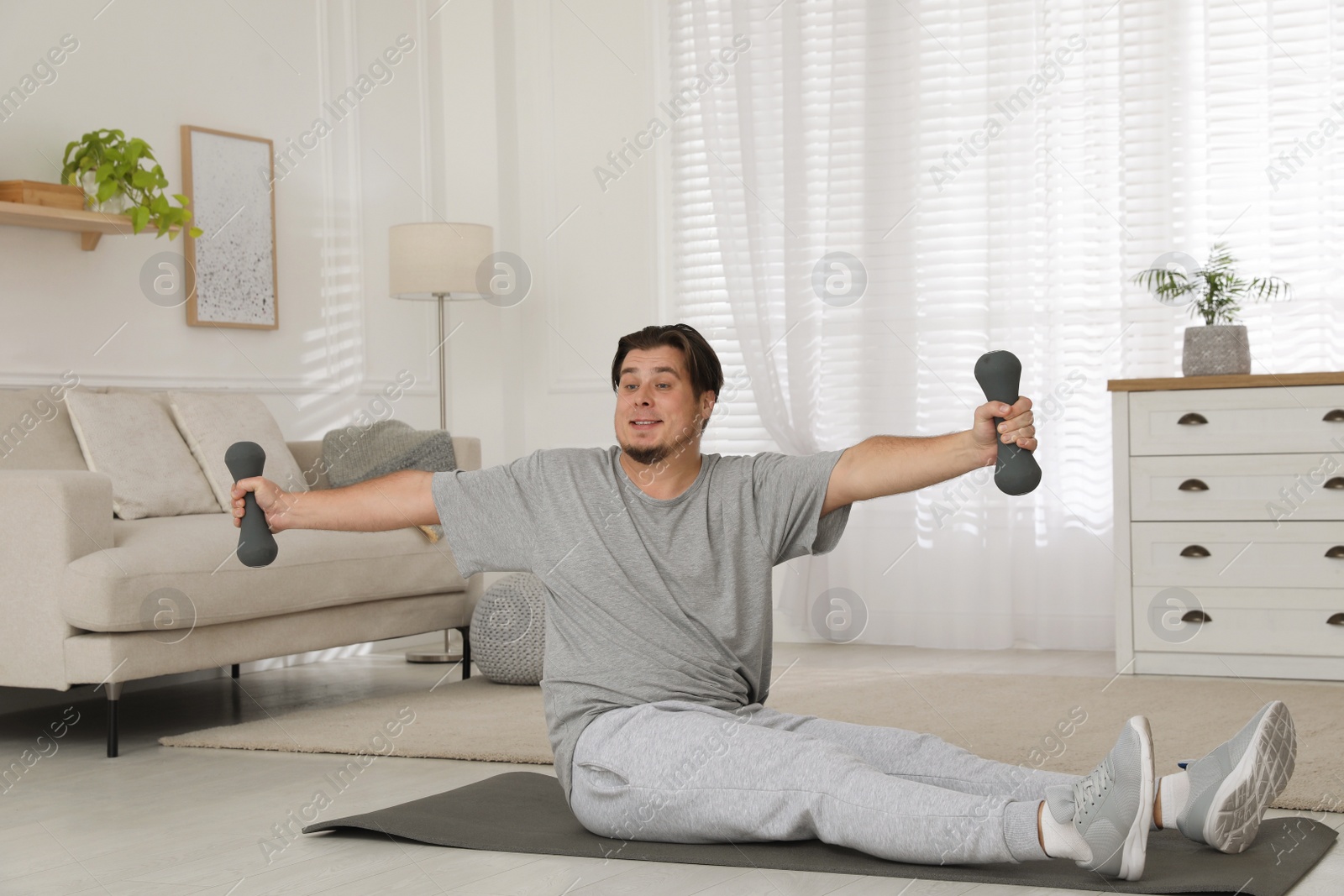 Photo of Overweight man doing exercise with dumbbells on mat at home