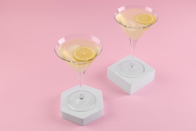 Photo of Martini glasses of cocktail with lemon slices on stands against pink background