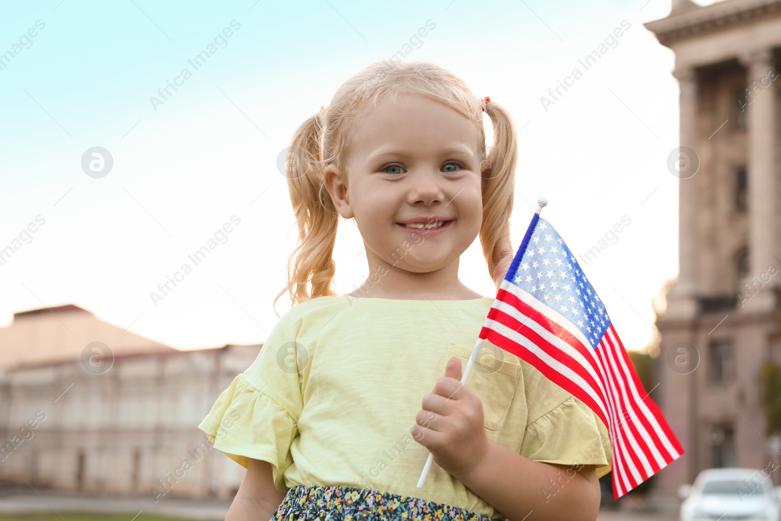 Photo of Cute little girl with American flag on city street