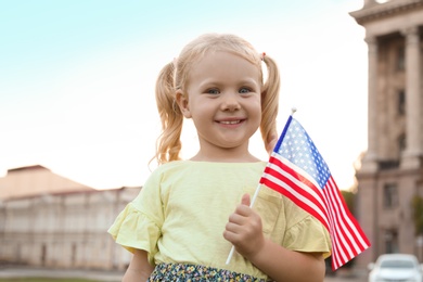 Cute little girl with American flag on city street