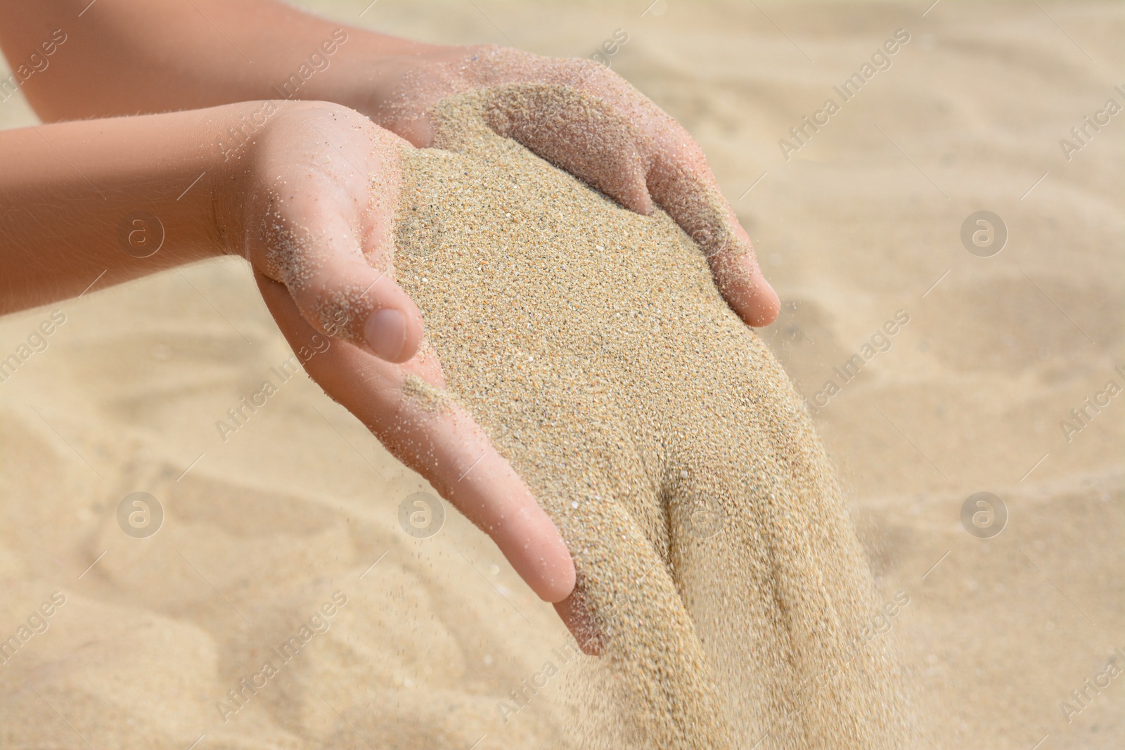 Photo of Child pouring sand from hands on beach, closeup. Fleeting time concept