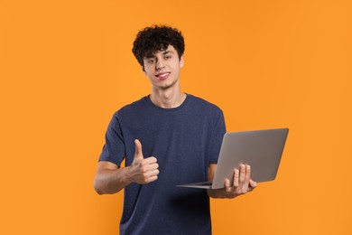 Handsome young man with laptop showing thumb up on orange background