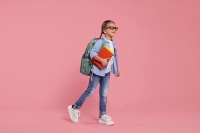 Photo of Happy schoolgirl in glasses with backpack and books on pink background