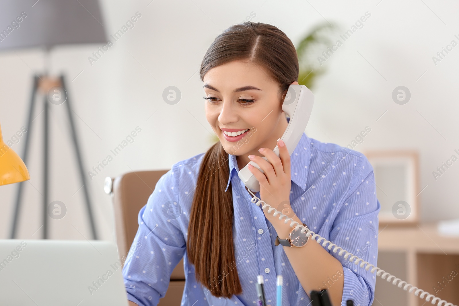 Photo of Young woman talking on phone at workplace