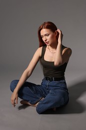 Beautiful young woman sitting on gray background