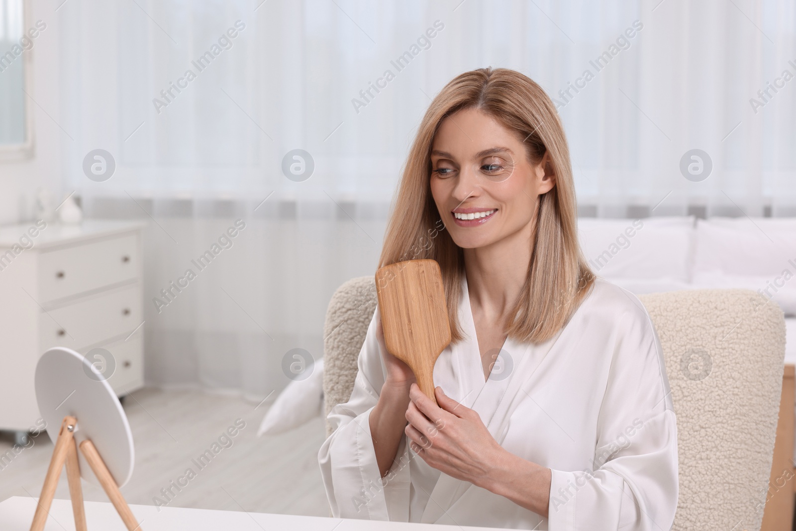 Photo of Beautiful woman brushing her hair at vanity in bedroom