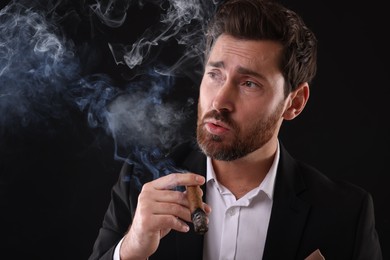 Photo of Handsome man in elegant suit smoking cigar on black background