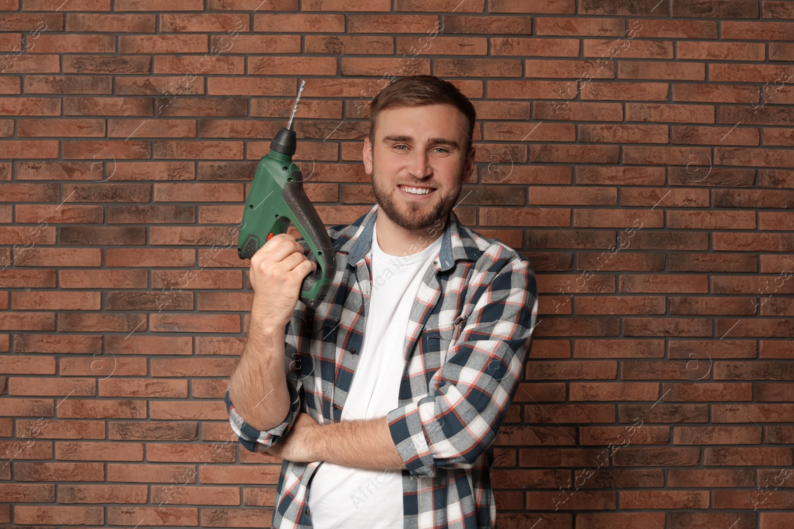 Photo of Young working man with modern electric drill near brick wall