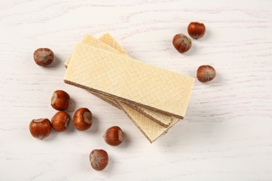 Delicious wafers with hazelnuts on white wooden background