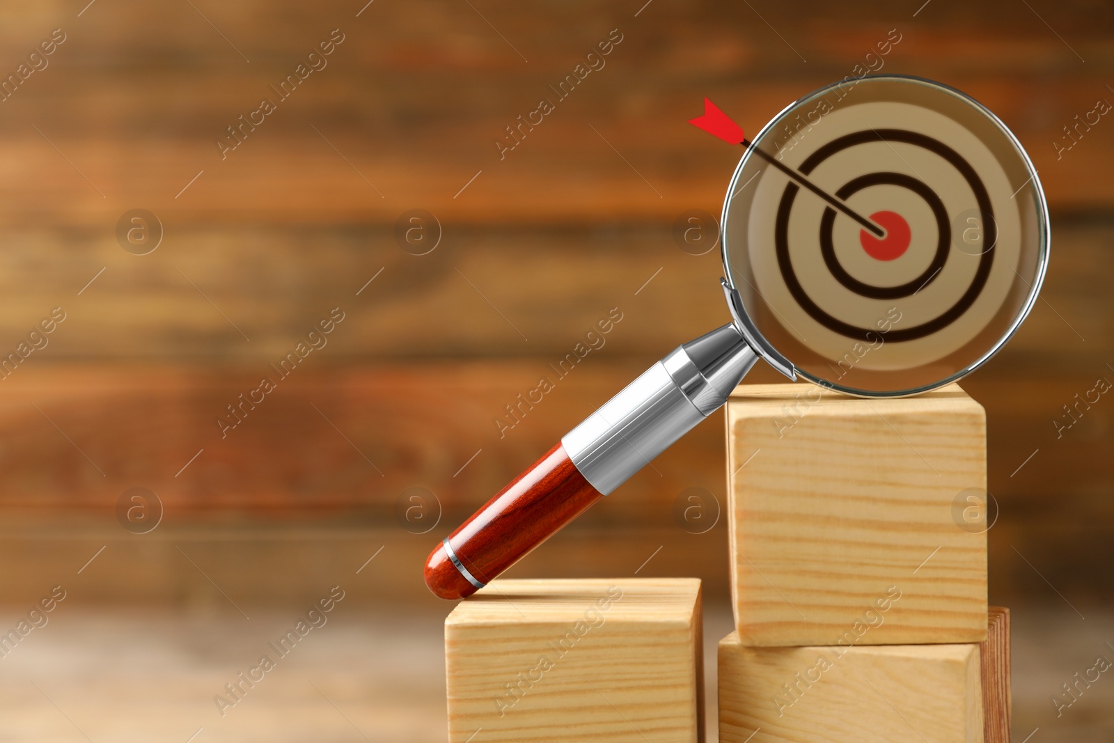 Image of Magnifying glass with illustration of target and arrow on wooden cubes against blurred background, space for text