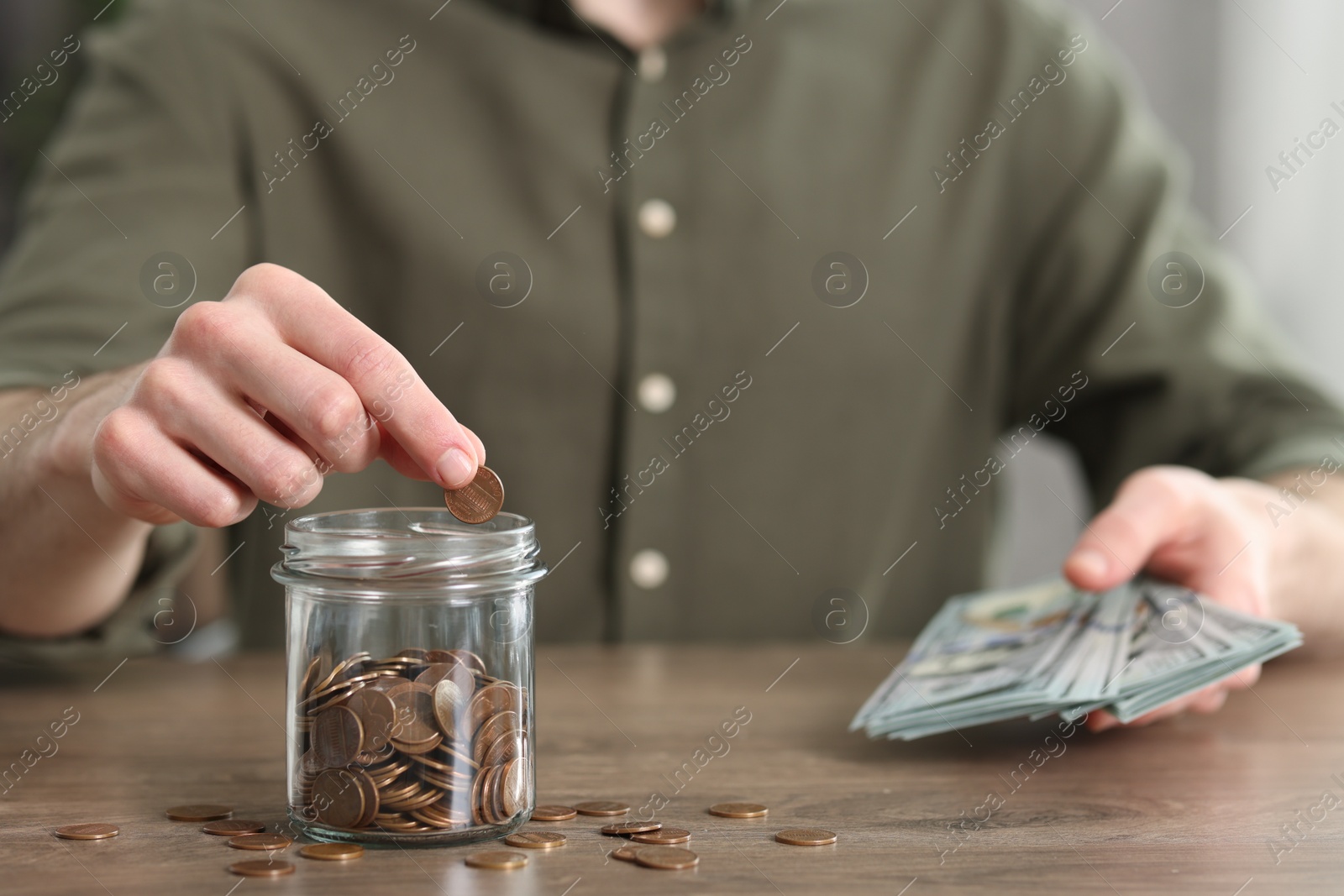 Photo of Financial savings. Man putting coin into glass jar at wooden table, closeup