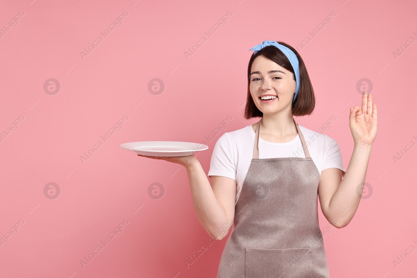 Photo of Happy confectioner with plate showing ok gesture on pink background, space for text