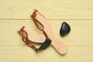 Photo of Slingshot with pebble on yellow wooden background, top view