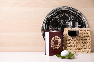 Photo of Symbolic Pesach (Passover Seder) items on white table against wooden background, space for text