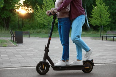 Photo of Couple riding modern electric kick scooter in park, closeup
