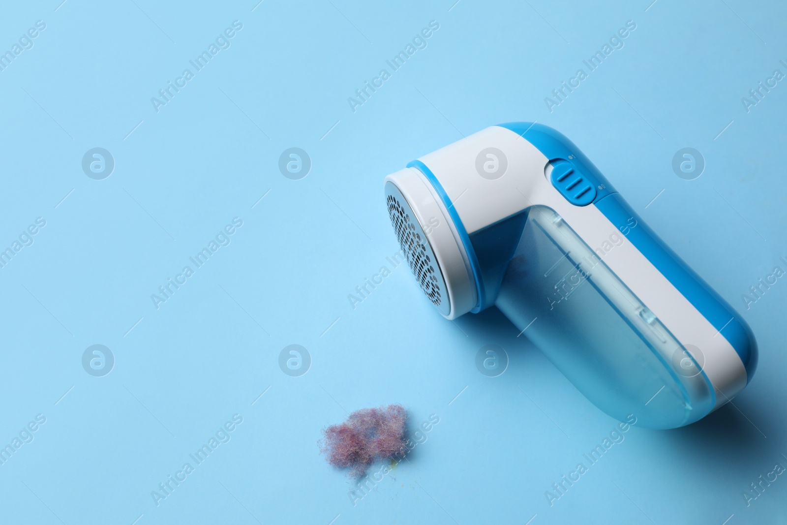 Photo of Modern fabric shaver and lint on light blue background. Space for text