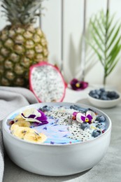 Delicious smoothie bowl with fresh fruits, blueberries and flowers on light grey table, closeup