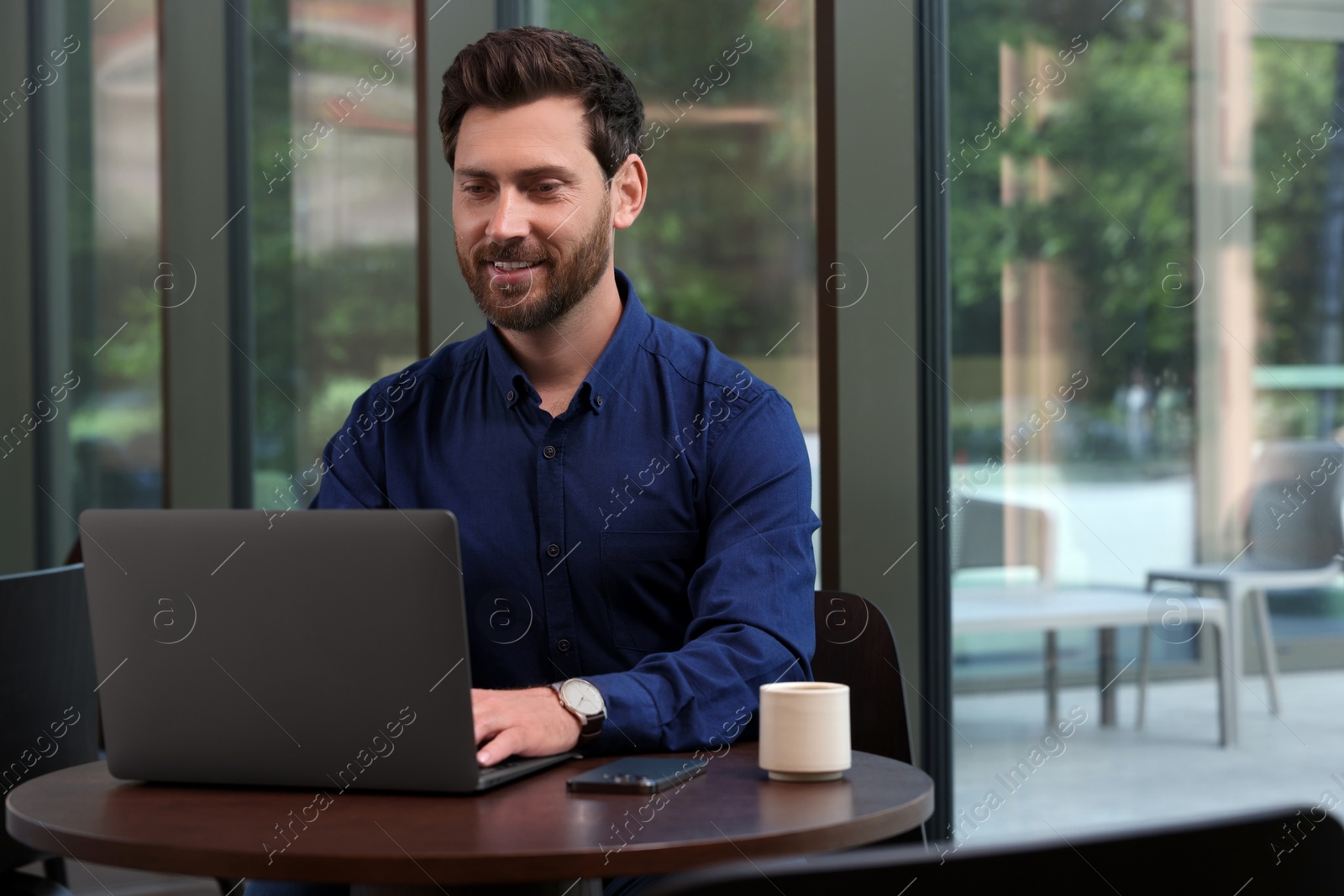 Photo of Man working on laptop at table in cafe