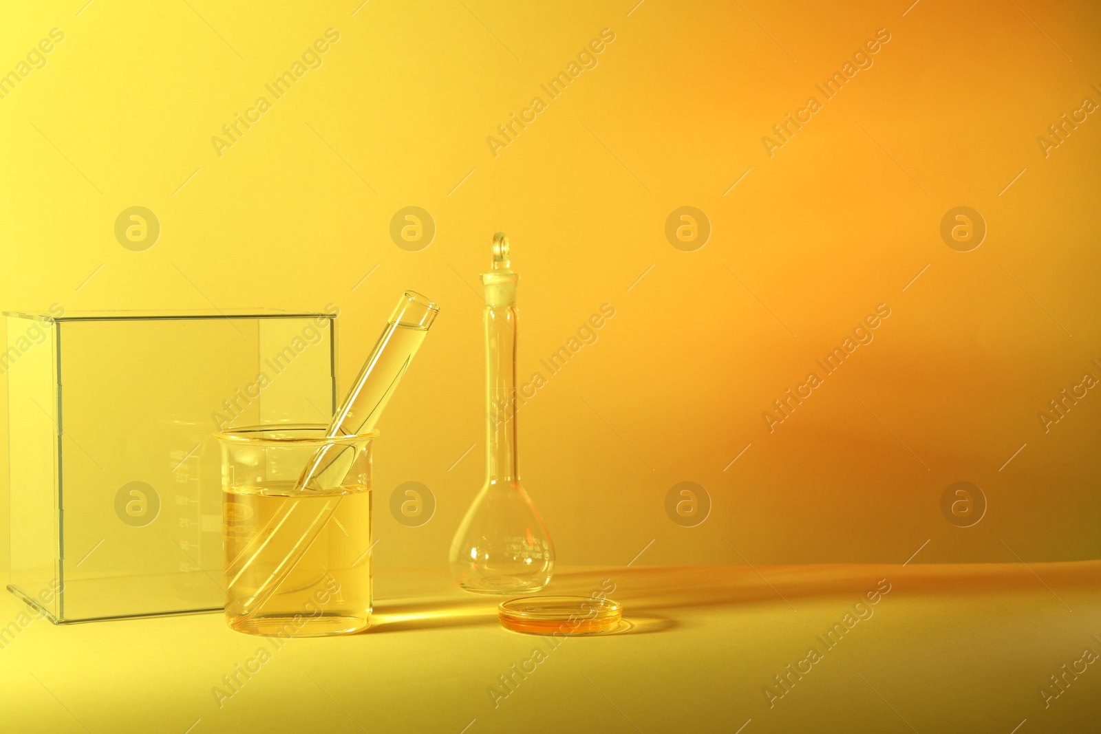 Photo of Laboratory analysis. Different glassware on table against yellow background, space for text