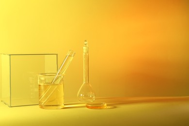 Photo of Laboratory analysis. Different glassware on table against yellow background, space for text