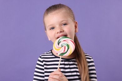Photo of Cute little girl licking colorful lollipop swirl on violet background