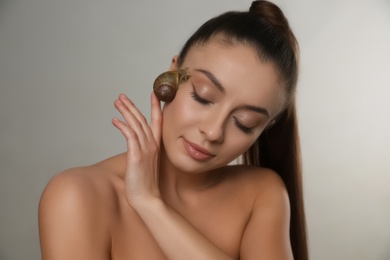 Photo of Beautiful young woman with snail on her face against grey background