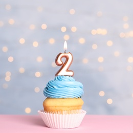 Photo of Birthday cupcake with number two candle on table against festive lights
