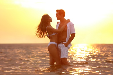 Happy young couple spending time together on sea beach at sunset