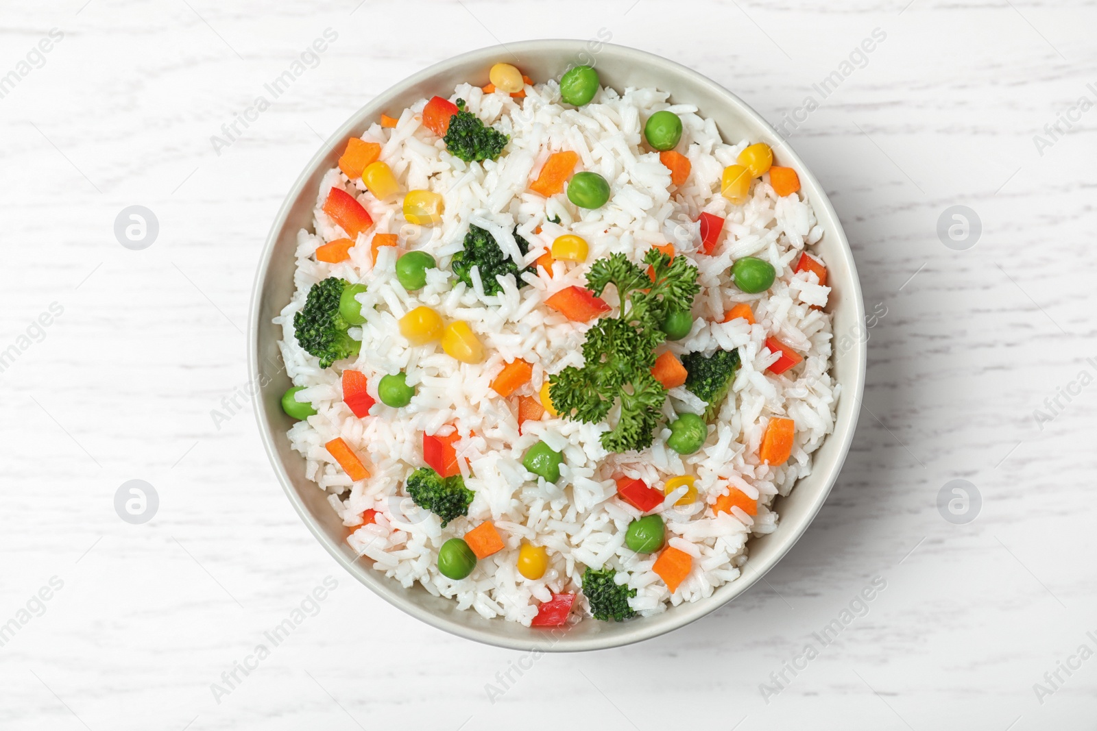 Photo of Bowl with tasty rice and vegetables on wooden background, top view