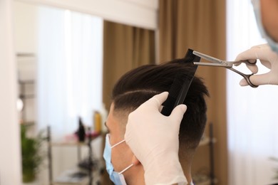 Photo of Professional stylist working with client in salon, closeup. Hairdressing services during Coronavirus quarantine