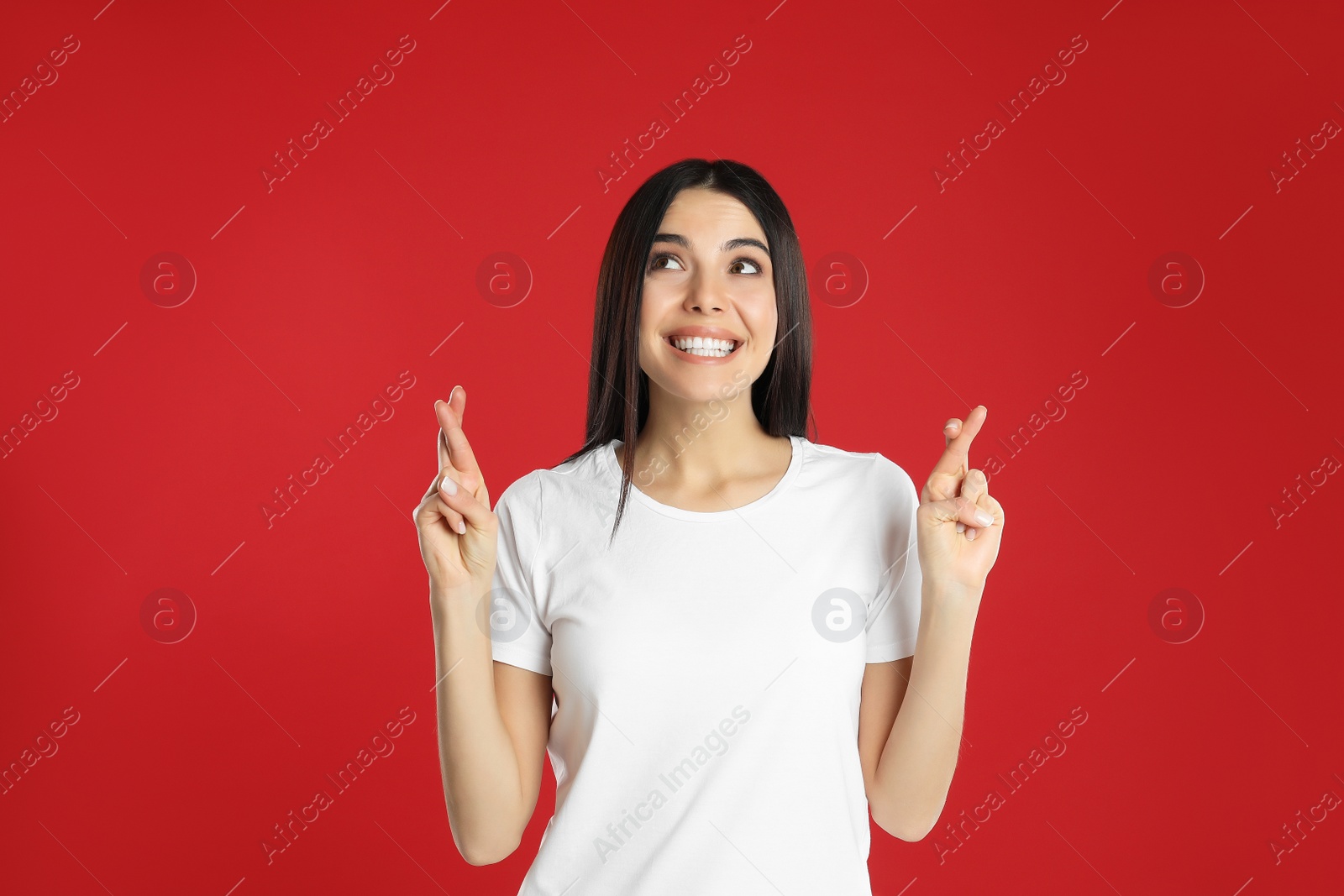 Photo of Woman with crossed fingers on red background. Superstition concept