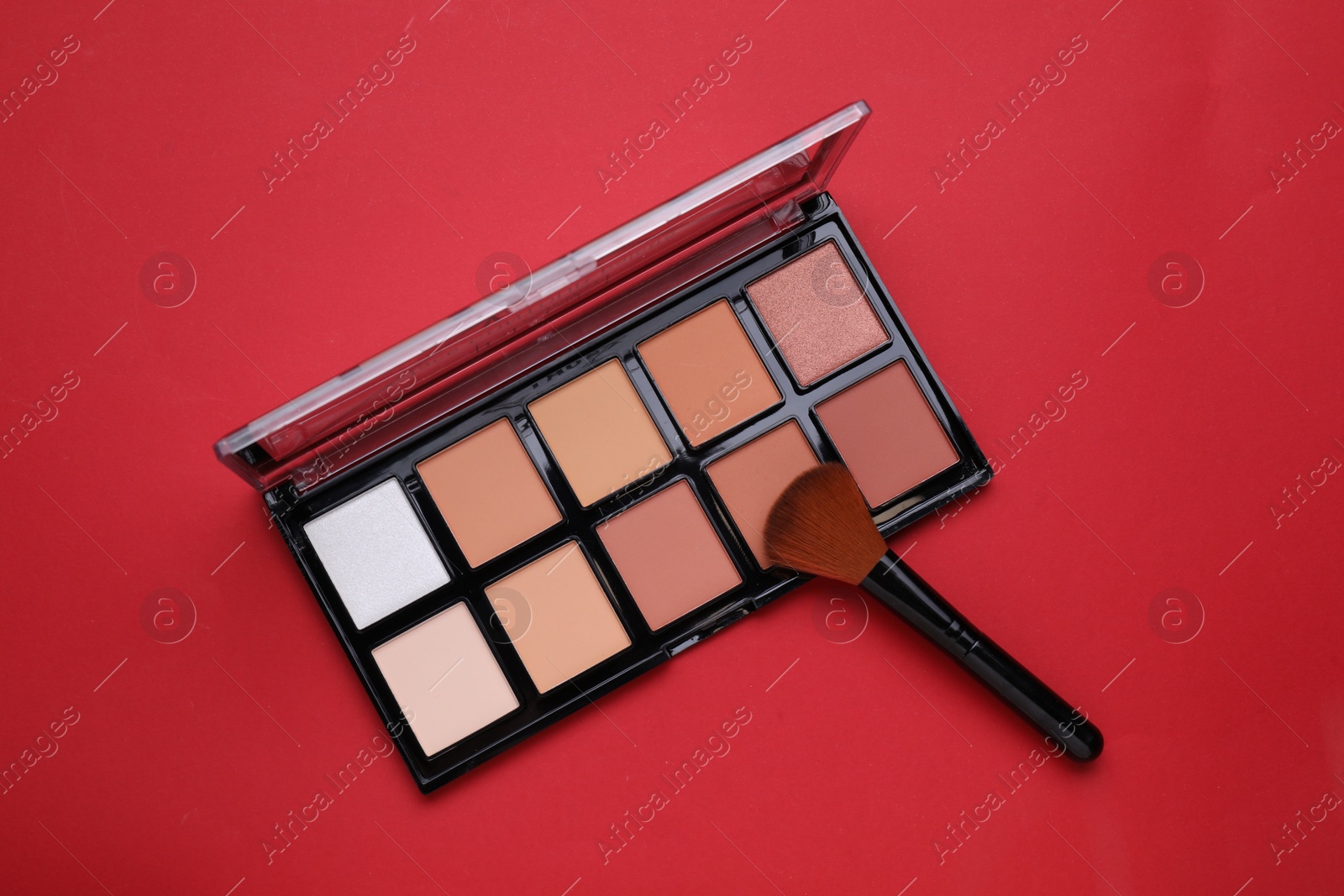 Photo of Colorful contouring palette with brush on red background, top view. Professional cosmetic product