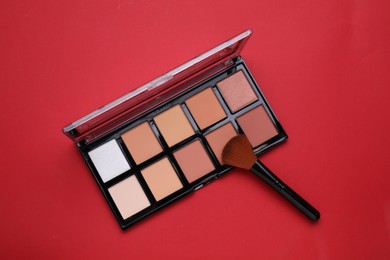 Colorful contouring palette with brush on red background, top view. Professional cosmetic product