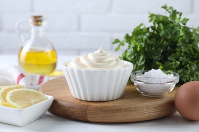 Photo of Fresh mayonnaise sauce in bowl and ingredients on table