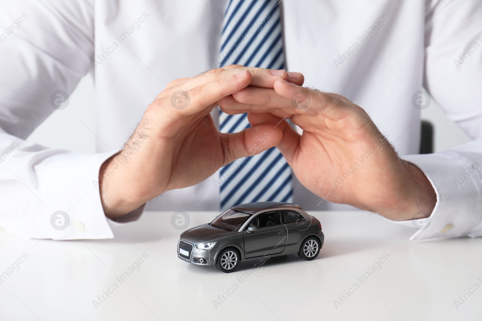 Photo of Male insurance agent covering toy car at table, closeup