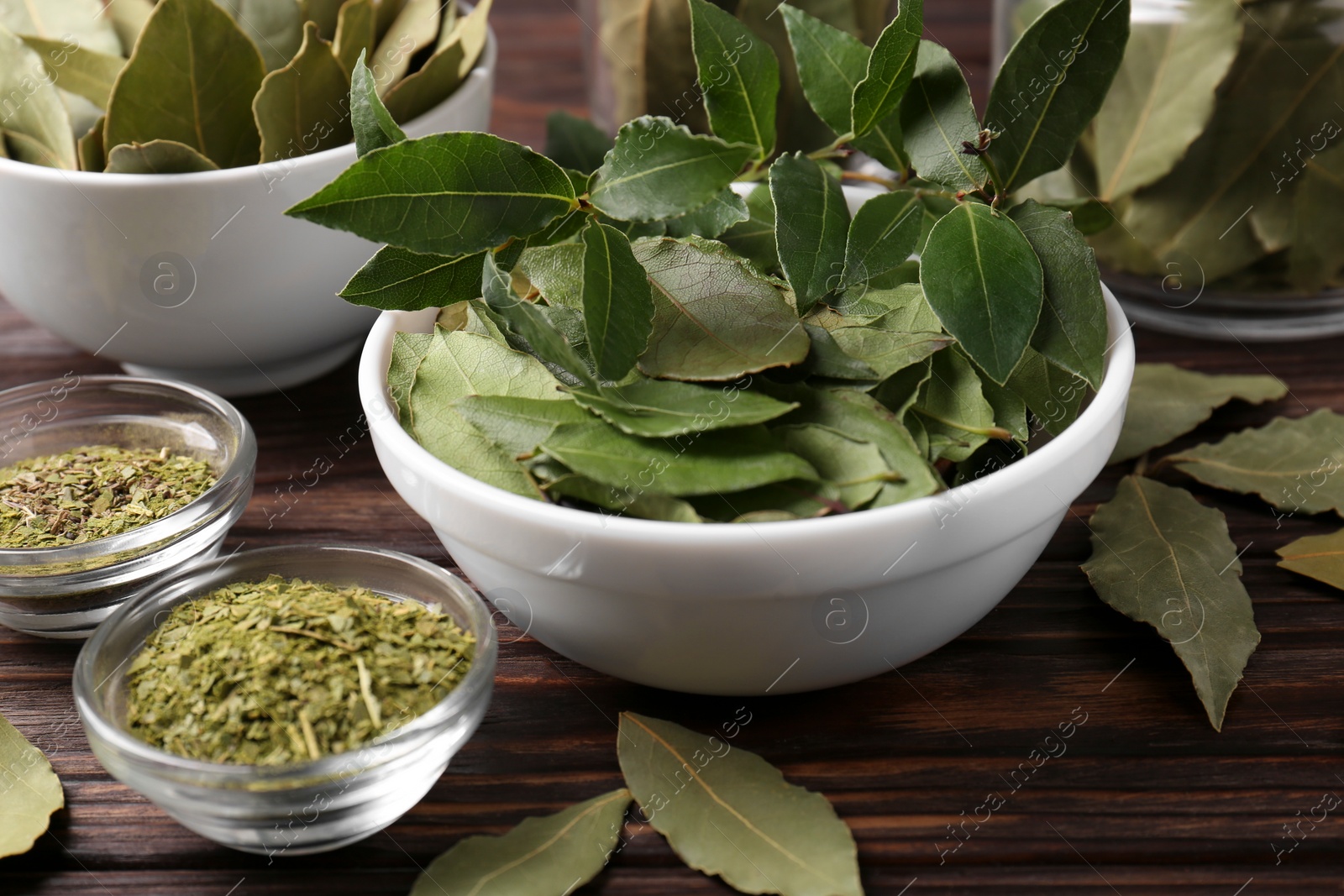 Photo of Bowl with ground, fresh and dry bay leaves on wooden table, closeup