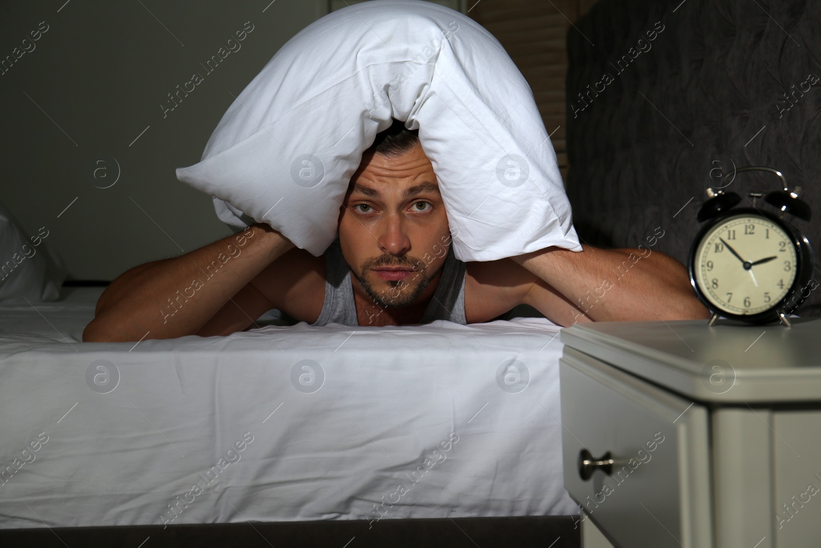 Photo of Man covering head with pillow in bed at home. Sleep disorder