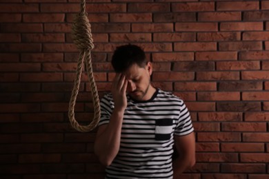 Photo of Depressed man near brick wall, focus on rope noose