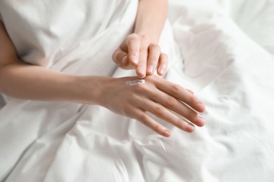 Photo of Woman applying hand cream in bed, closeup