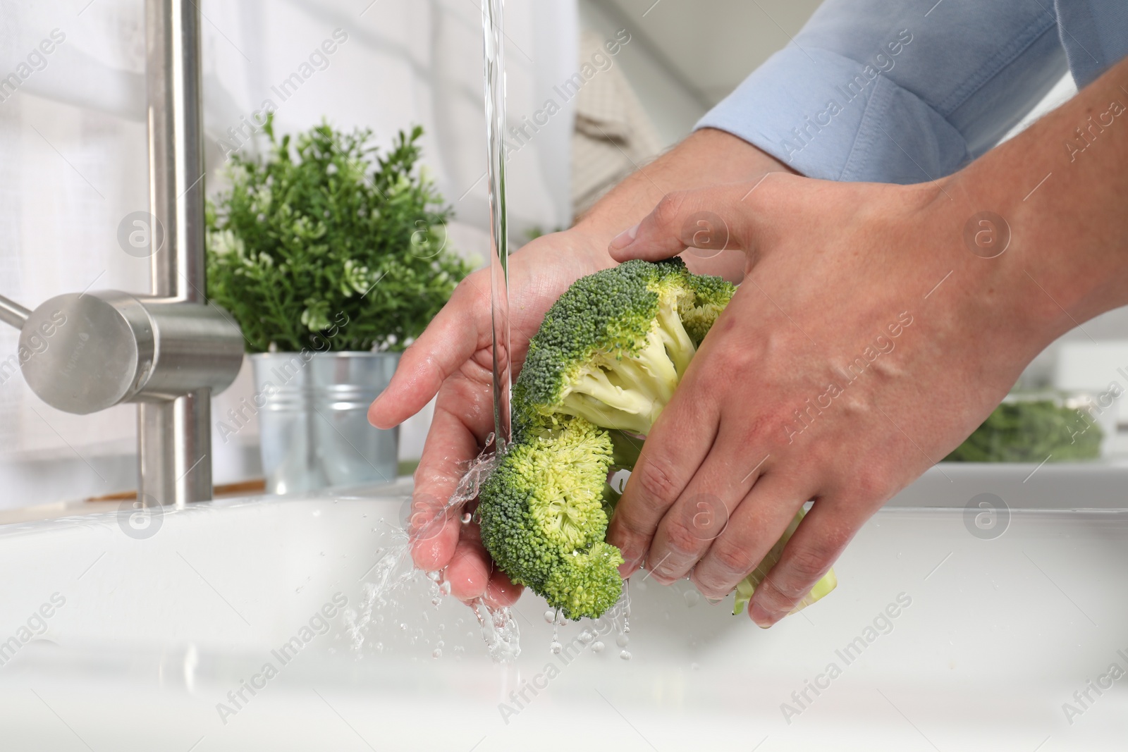 Photo of Man washing fresh broccoli in kitchen, closeup