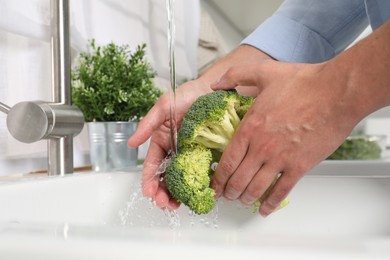 Photo of Man washing fresh broccoli in kitchen, closeup