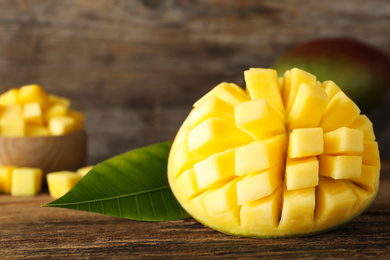 Photo of Half of ripe mango cut into cubes on wooden table