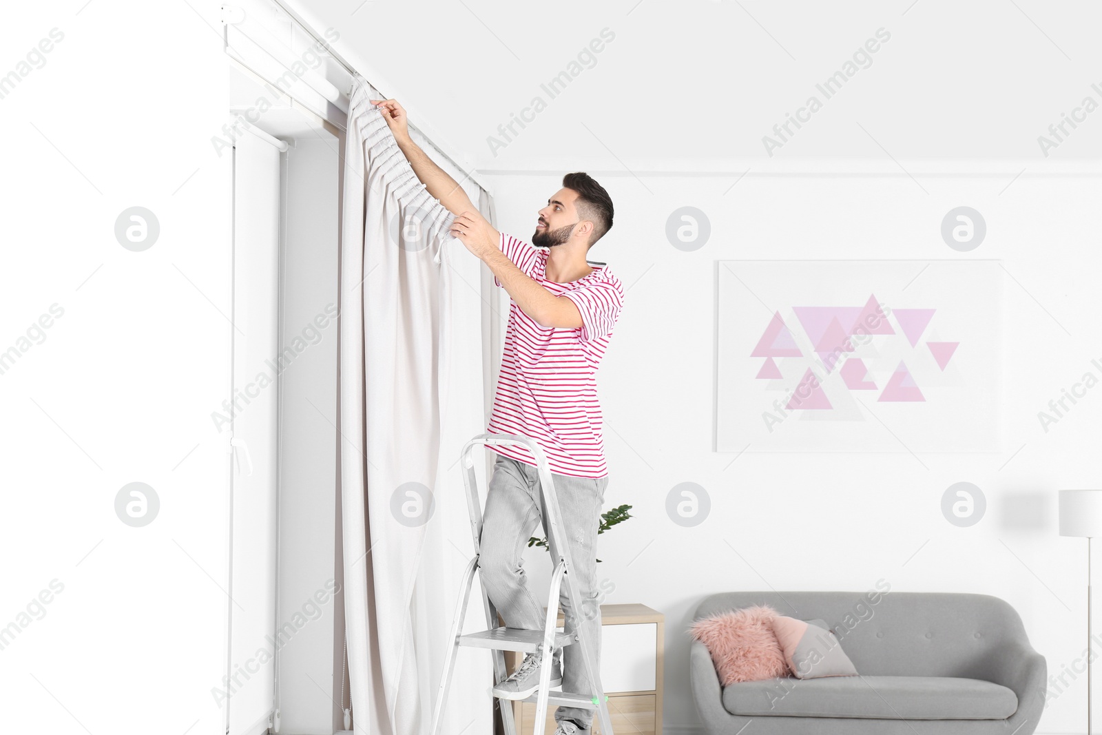 Photo of Young man hanging window curtain in room. Space for text