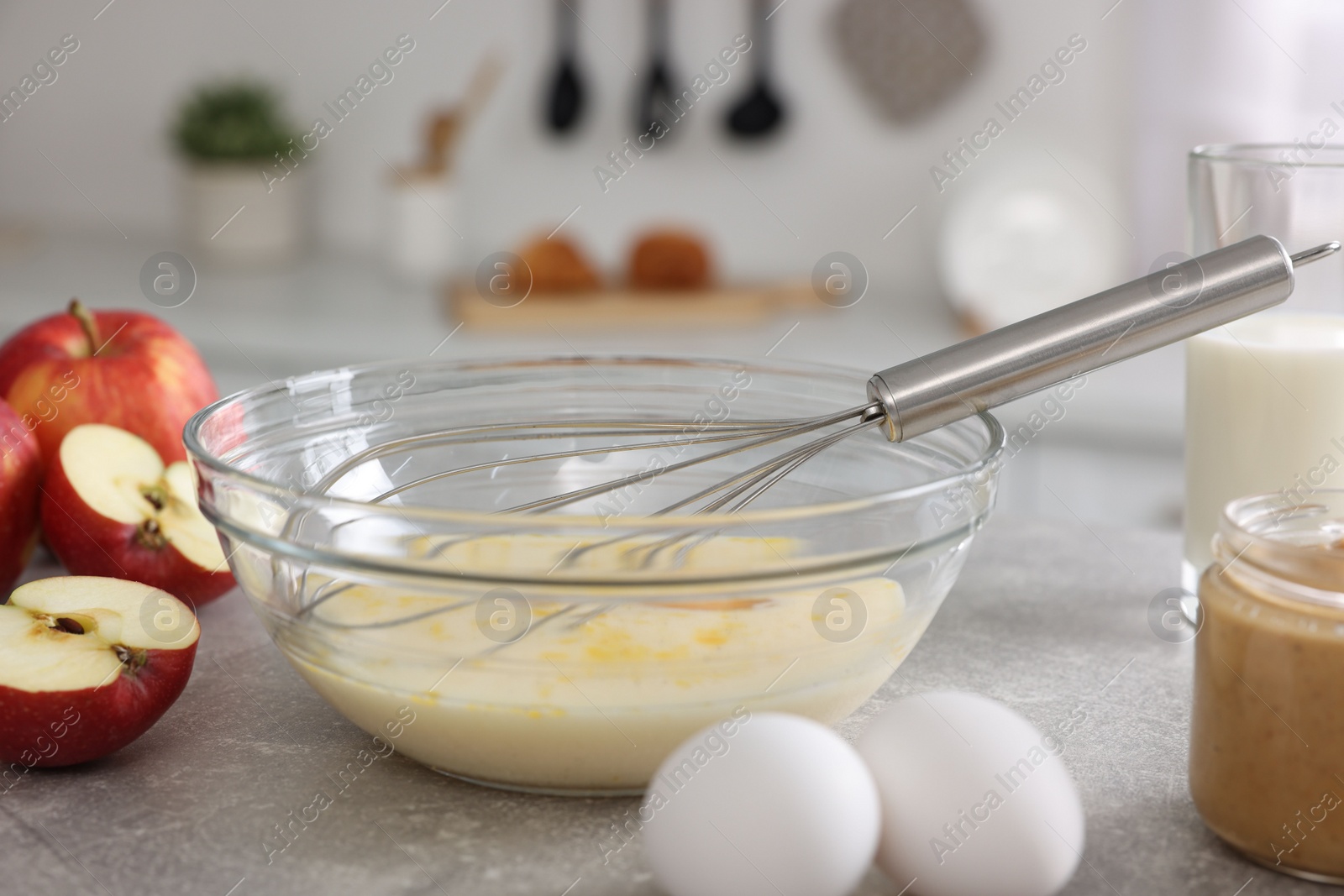 Photo of Whisk, bowl, beaten eggs and other ingredients on grey table indoors