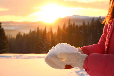 Photo of Woman holding pile of snow outdoors, closeup. Winter vacation