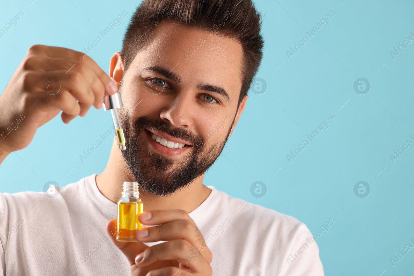 Photo of Handsome man with cosmetic serum in hands on light blue background, space for text